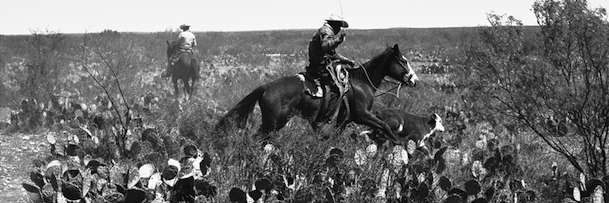 Black and white photo of two cowboys on horseback in the desert
